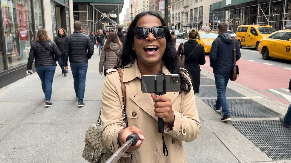 Devin Halbal holding a selfie stick and smiling while walking in a city